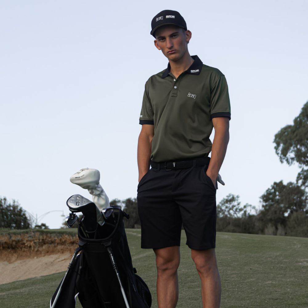 Man wearing a Birdie Assassin golf polo next to his golf bag with his hands in his pocket.