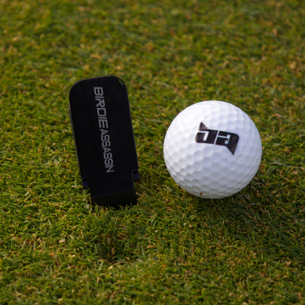 Birdie Assassin divot tool repairing a divot on a putting green next to a golf ball