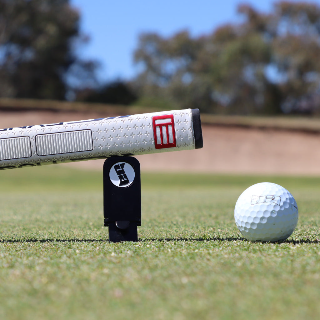 Birdie Assassin divot tool with a golf club leaning on it next to a golf ball