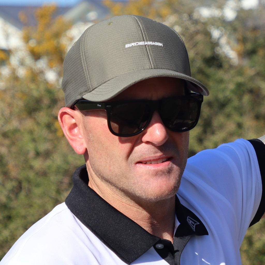 Man wearing a Green Birdie Assassin Players Golf Cap and sunglasses on a golf course