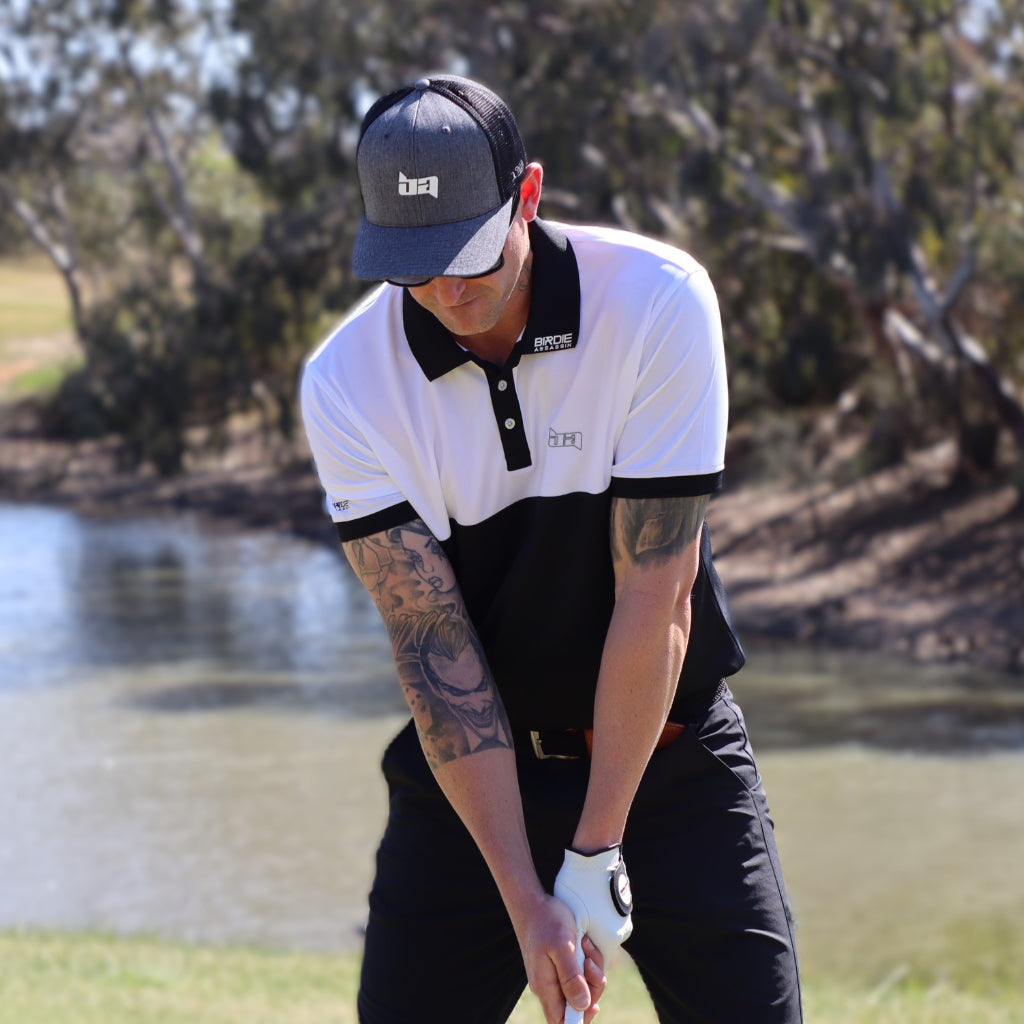 Golfer with a Bond golf polo from Birdie Assassin preparing to hit a shot on a golf course with trees and water in the background.