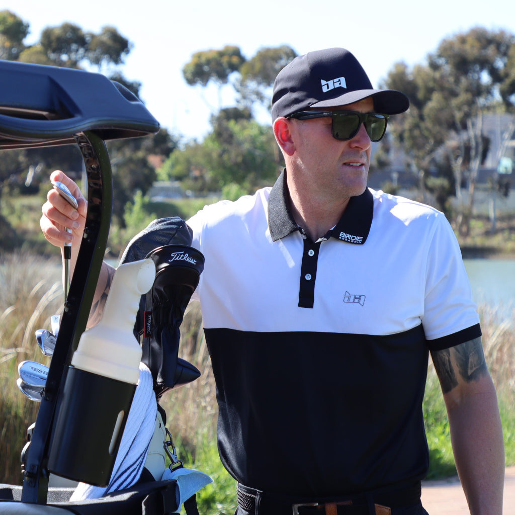 Man in a Bond golf polo from Birdie Assassin standing next to a golf cart on a golf course
