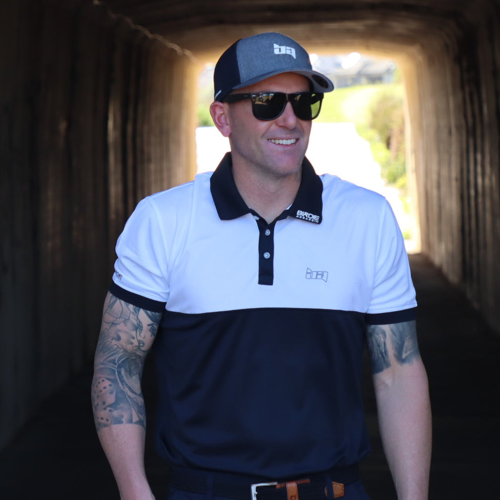 Man wearing a Bond golf polo shirt from Birdie Assassin with sunglasses and a cap, standing in a tunnel.