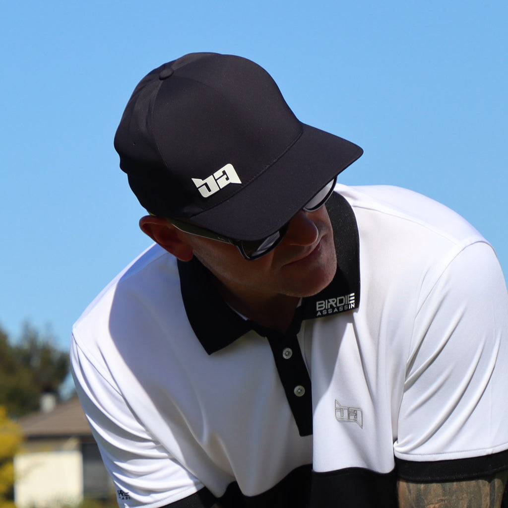 Person wearing a black Delta golf cap from Birdie Assassin and white shirt with brand logos against a clear blue sky.