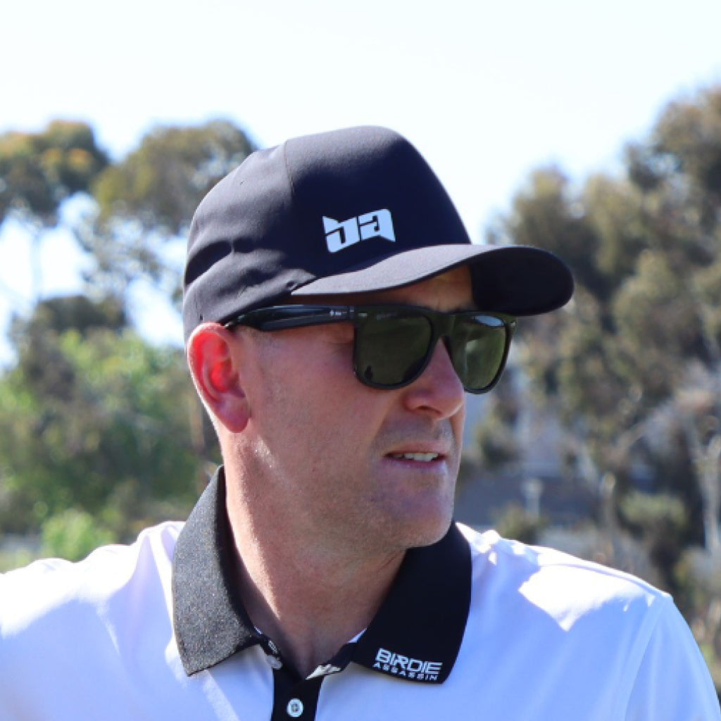 Man wearing a Delta golf cap from Birdie Assassin and sunglasses with a blurred natural background