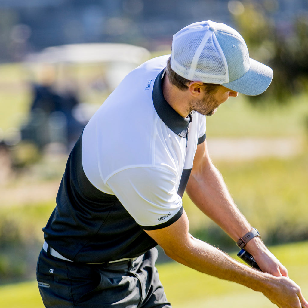 Golfer in action on a golf course wearing a Bond golf polo from Birdie Assassin with a grey and white golf  cap.