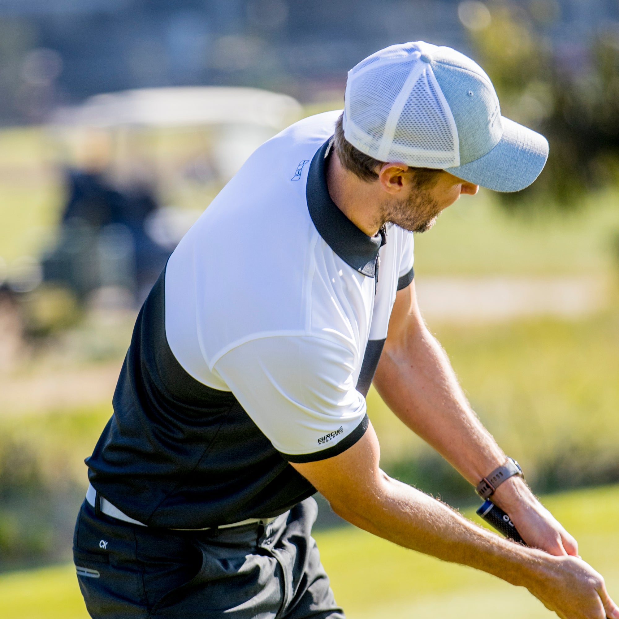 Golfer in action on a golf course wearing a Bond golf polo from Birdie Assassin with a grey and white golf  cap.