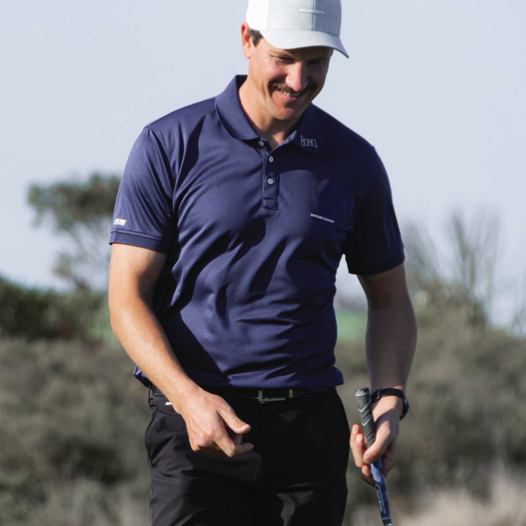 Man in a Bourne golf polo from birdie assassin. with a golf club and white hat