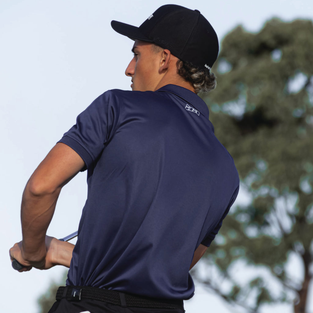 Man in a Bourne golf polo from birdie assassin and a black hat swinging a golf club