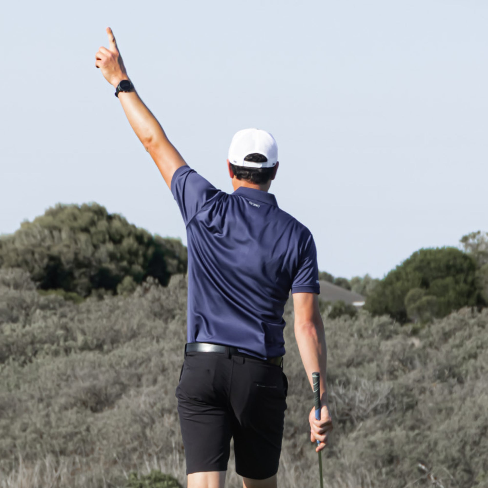 Golf player in a Bourne golf polo from Birdie Assassin pointing to the sky and celebrating on a golf course