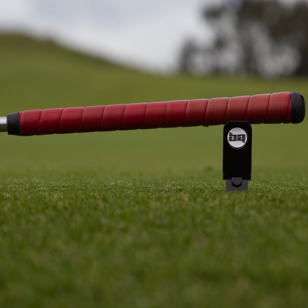 Birdie Assassin divot tool with a red handled golf club leaning on  it.