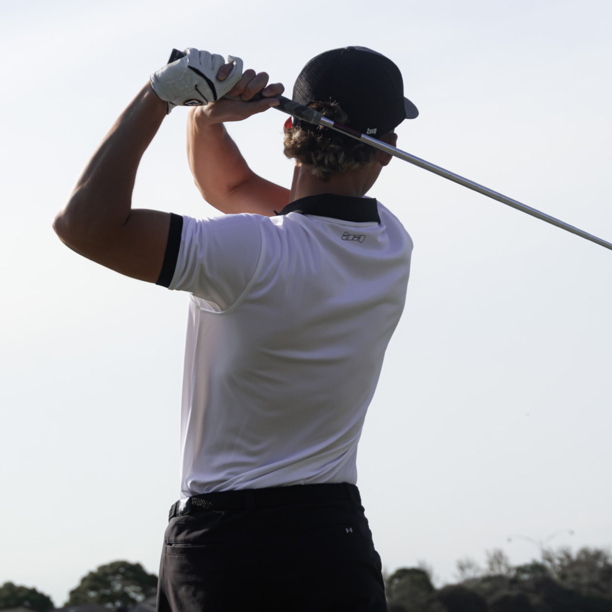 Golfer wearing an Iceman golf polo in mid-swing on a golf course with a clear sky.