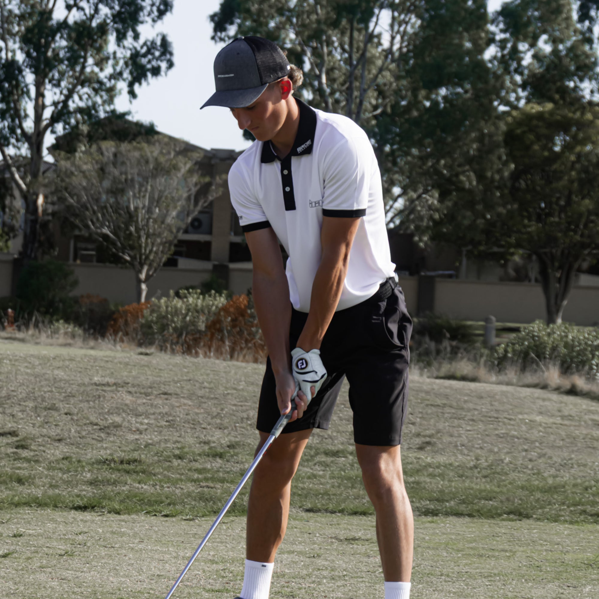 Person wearing a Iceman golf polo playing golf on a grassy course with trees in the background