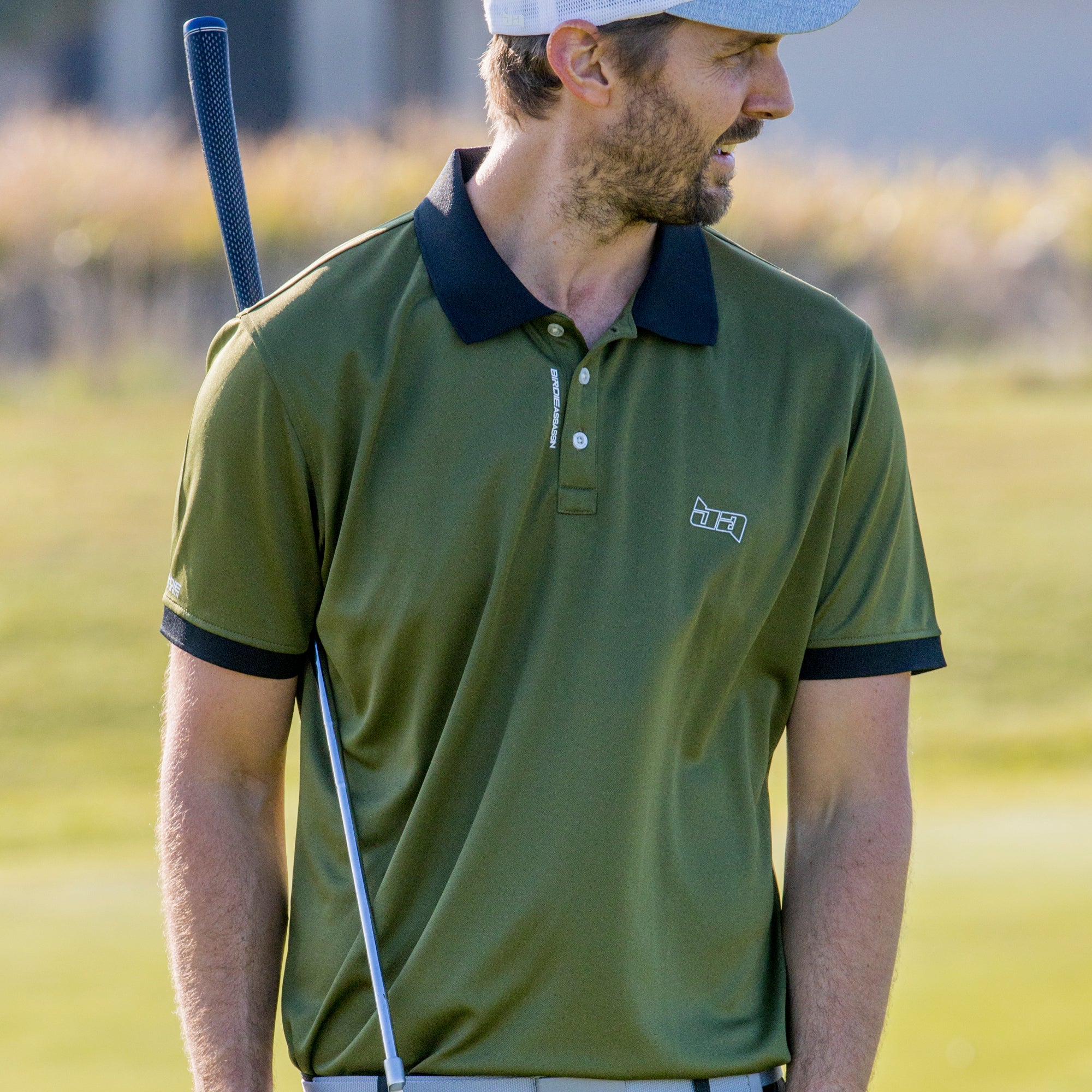 Man in a Marksman golf polo shirt from Birdie Assassin holding a golf club on a golf course