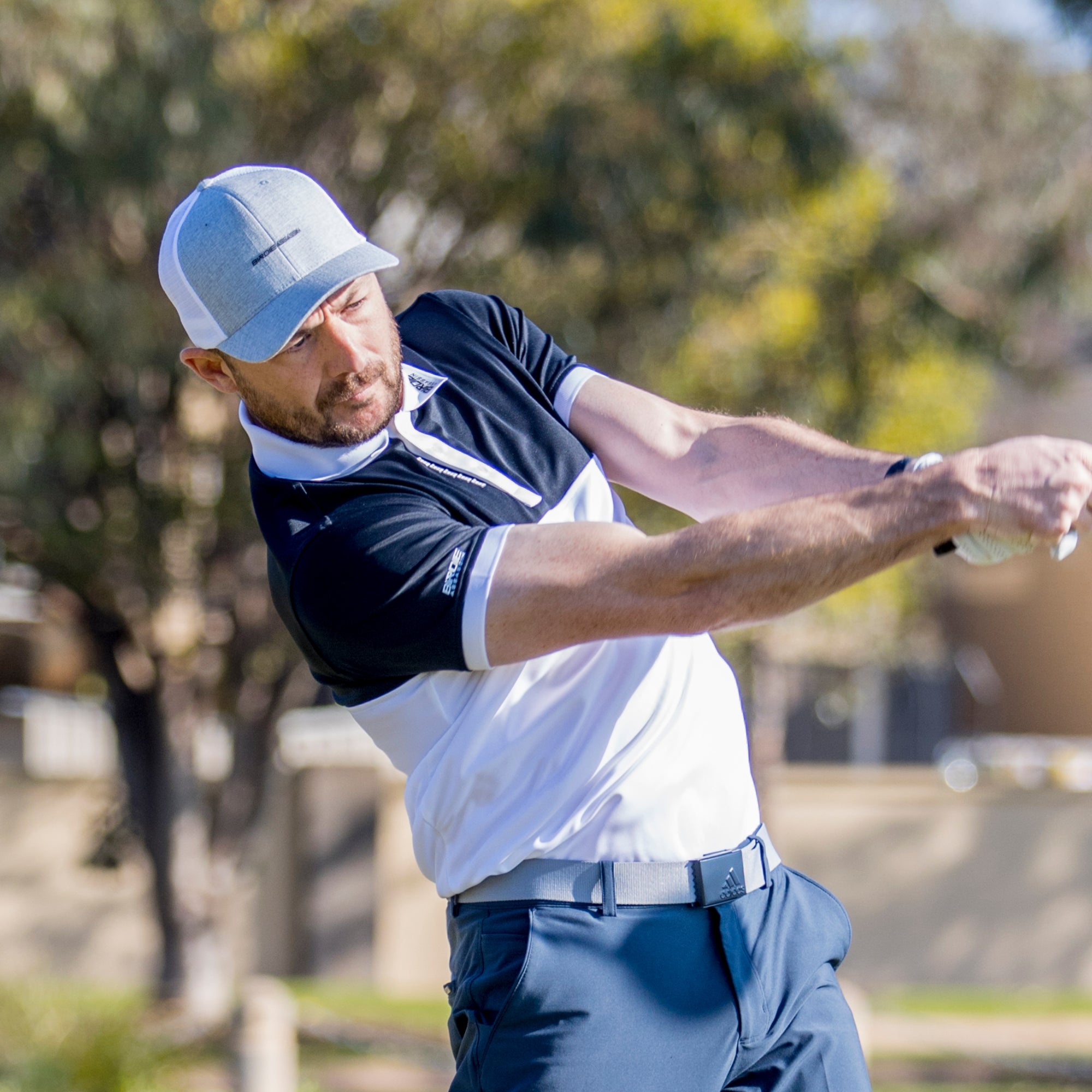 Man in a Yakuza golf polo from Birdie Assassin hitting a drive off a tee on a golf course 