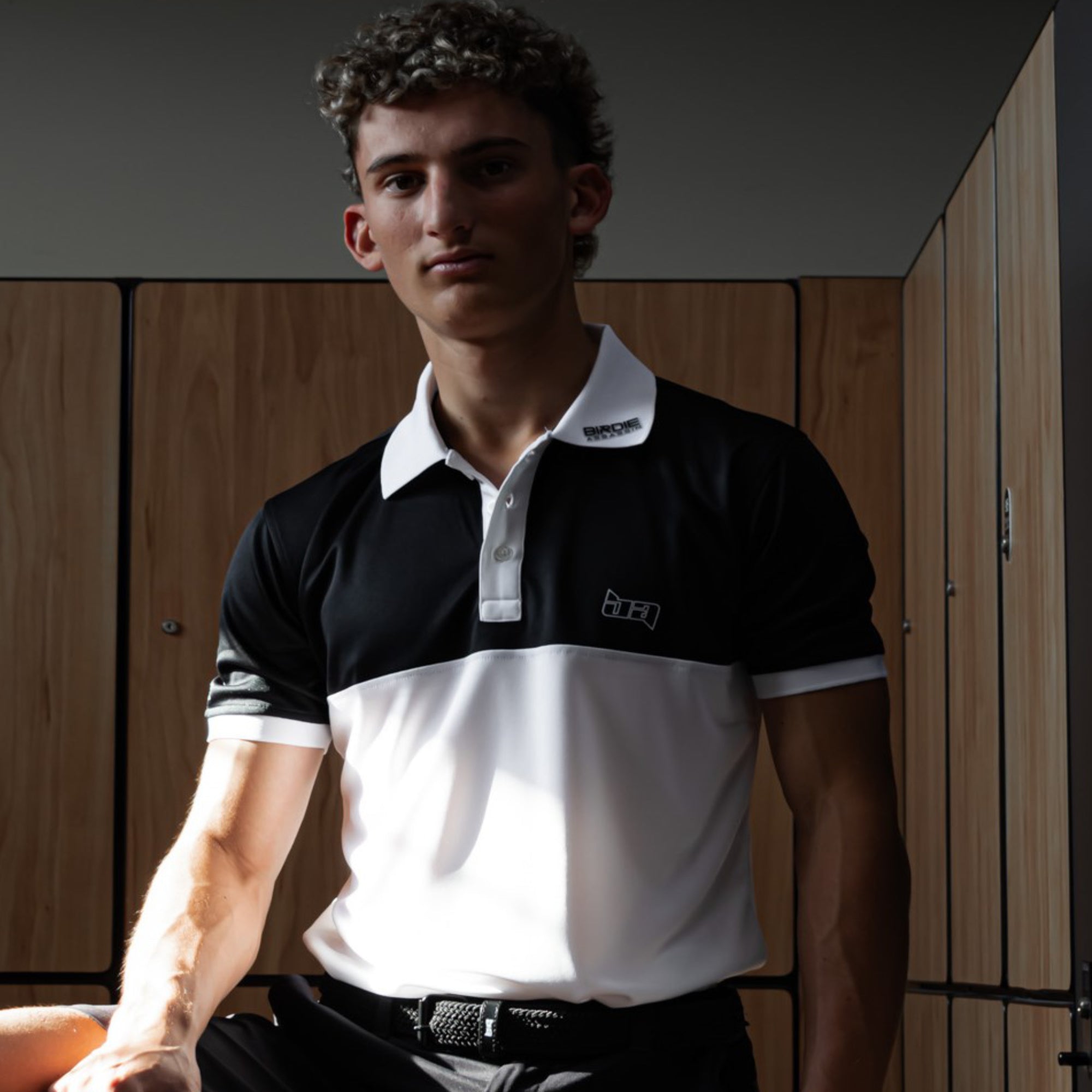 Man wearing a Yakuza golf polo shirt from Birdie Assassin sitting in a locker room.